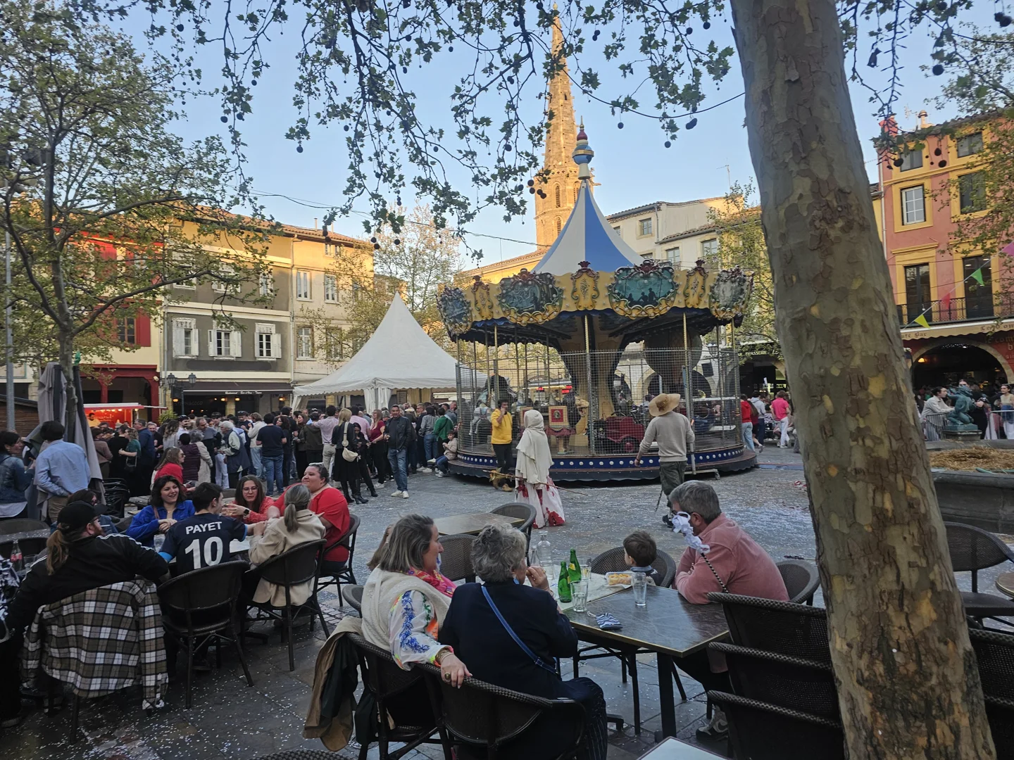 Lively Place de la République in Limoux, with terraces, a carousel and colourful historic façades in sunlight